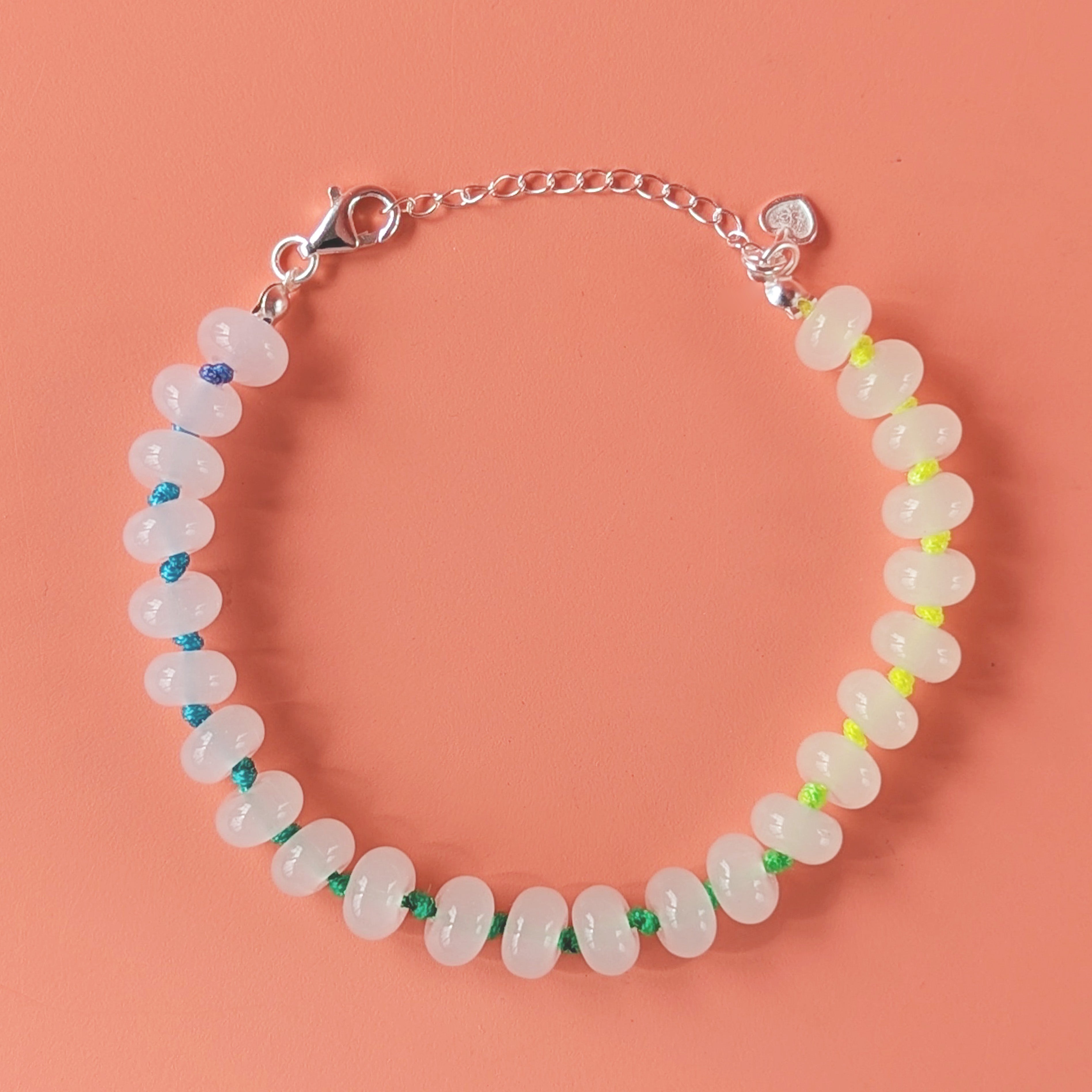 A beaded bracelet made of translucent white oval beads strung on a silver chain with a lobster clasp and extension chain, photographed on a solid peach background.