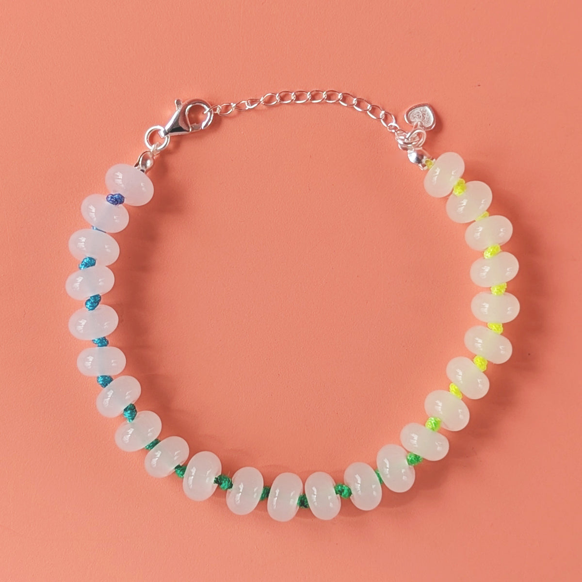 A beaded bracelet made of translucent white oval beads strung on a silver chain with a lobster clasp and extension chain, photographed on a solid peach background.