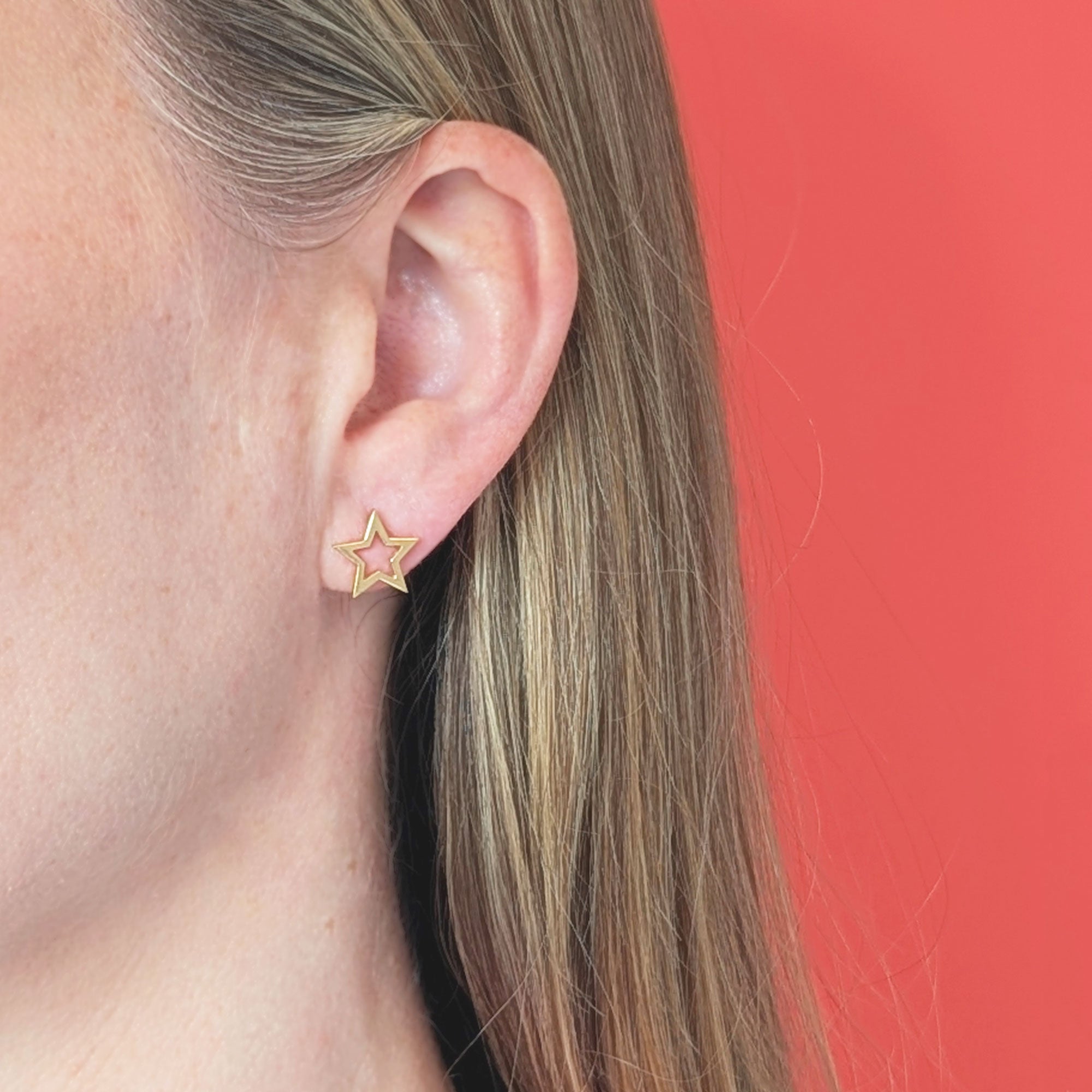 Gold star stud earring worn by a person with a coral background