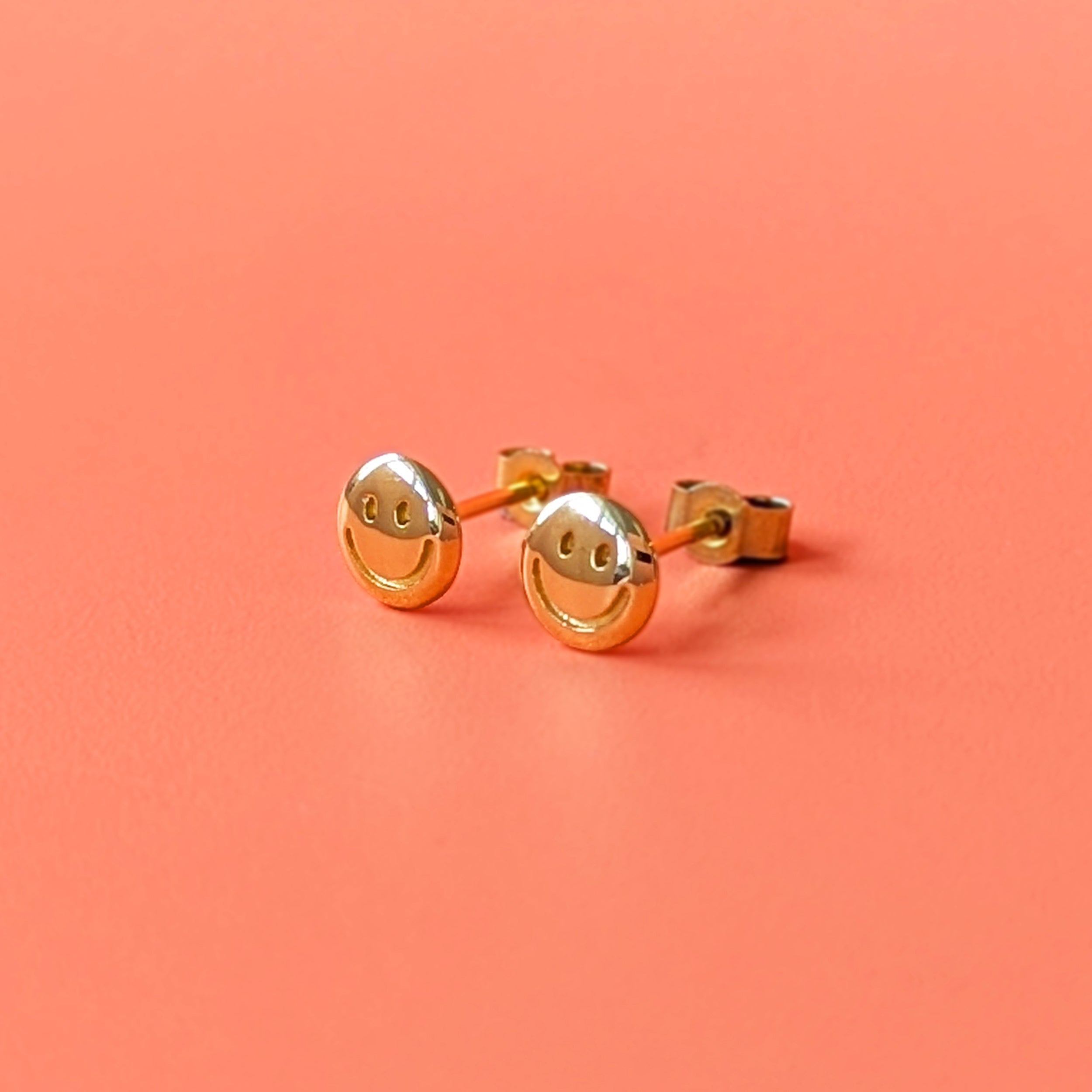 Gold happy face earrings on a coral background