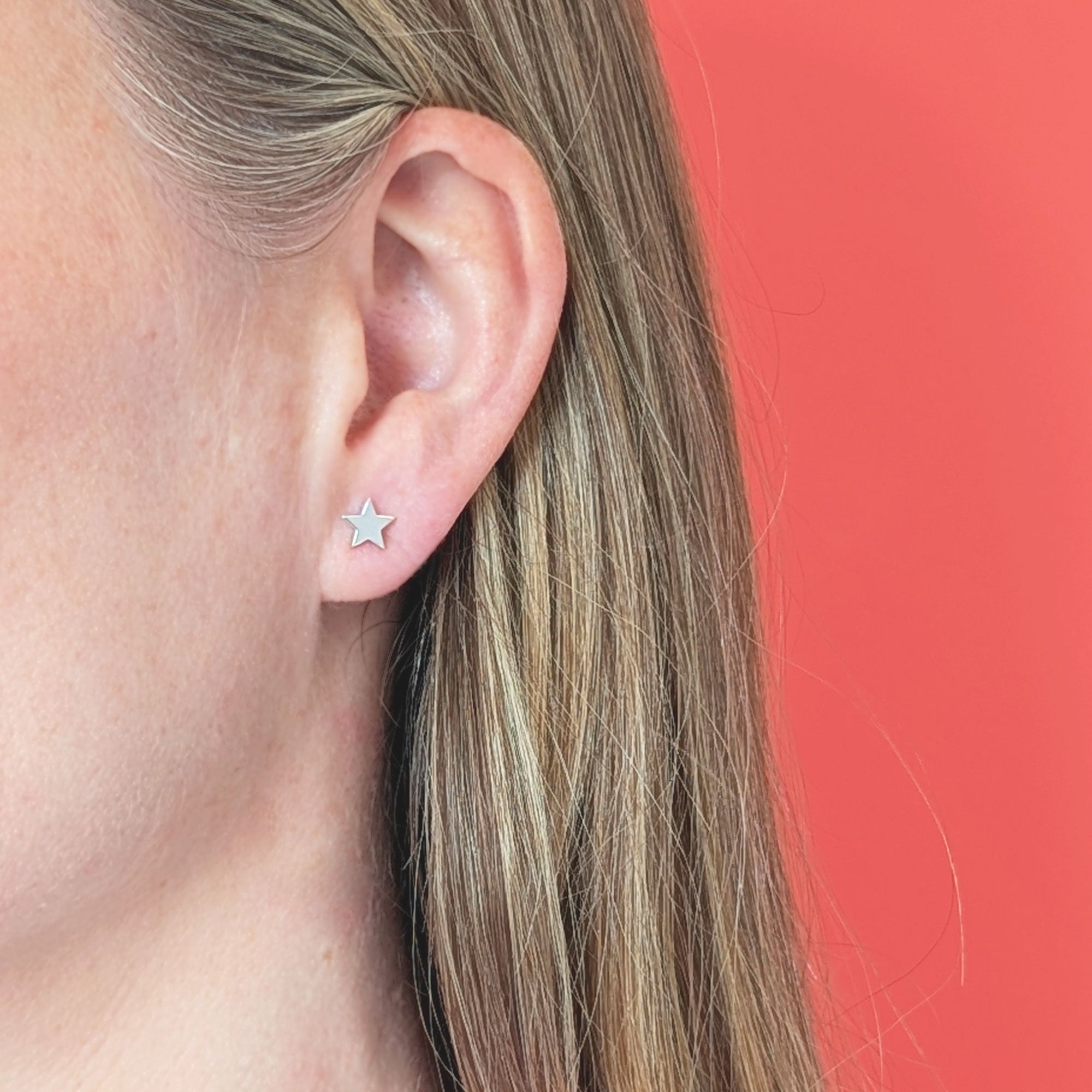 Star-shaped earring worn by a person with a coral background